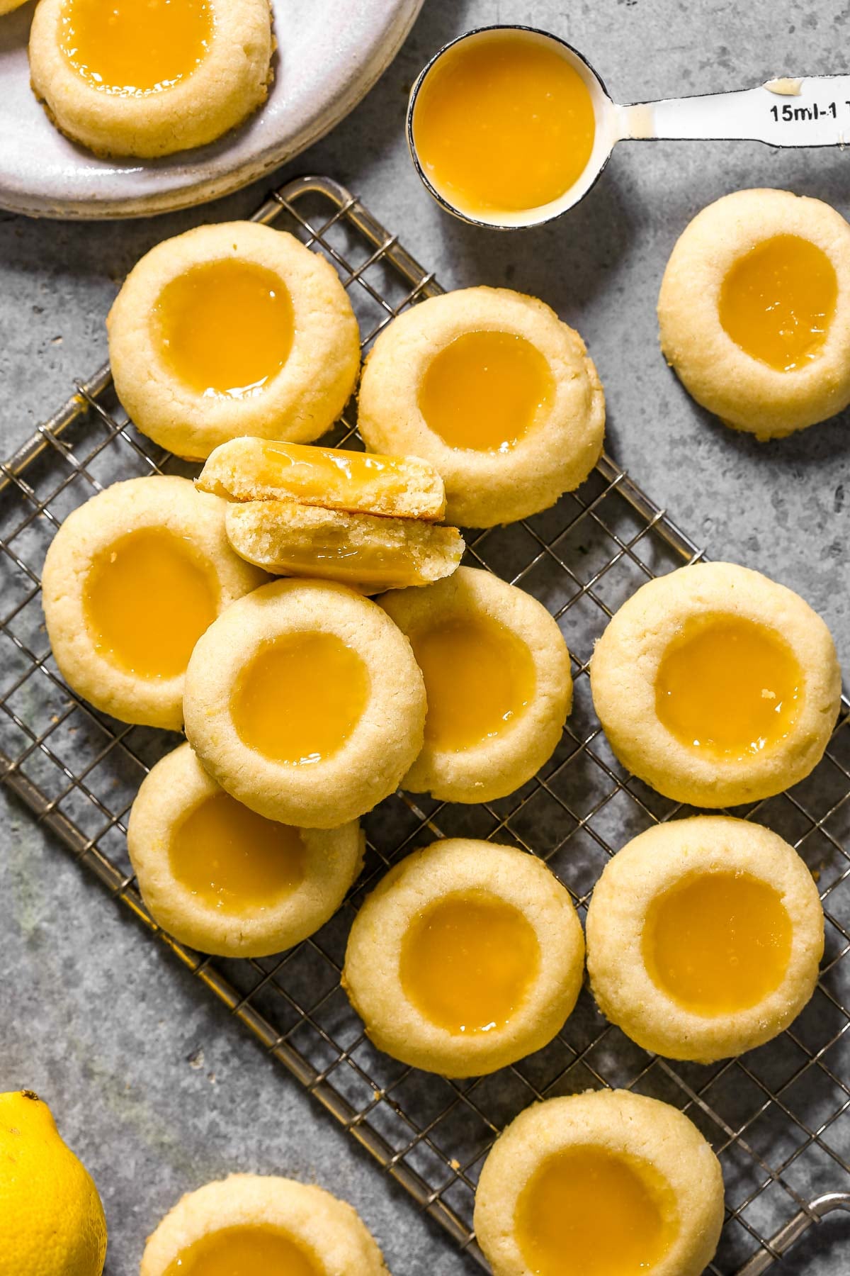 Thumbprint cookies with lemon curd filling on a cooling rack, with a measuring spoon and lemon nearby.