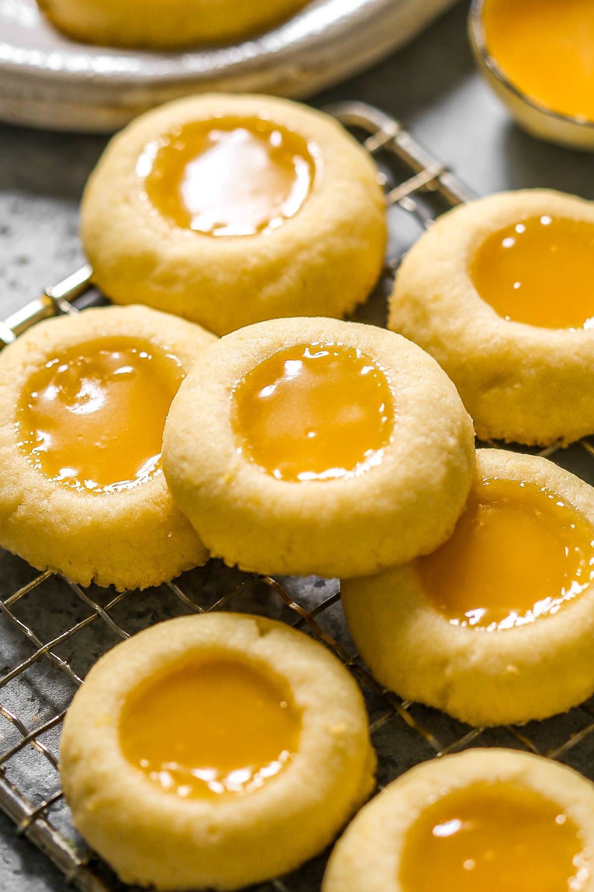Round thumbprint cookies filled with glossy yellow lemon curd, arranged on a cooling rack.