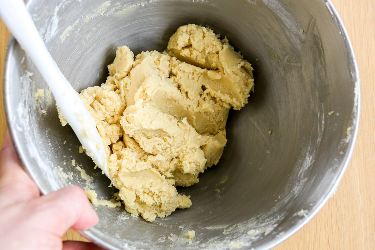 Thick lemon cookie dough batter in a metal mixing bowl with a white spatula set in it.