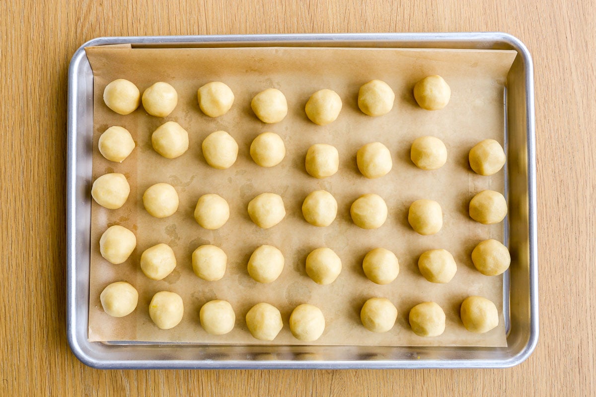 Lemon cookie dough rolled into balls and set on a parchment paper-lined baking sheet.