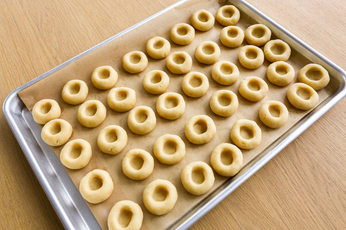 Cookie dough balls with thumb indentations set on a parchment-lined baking sheet.