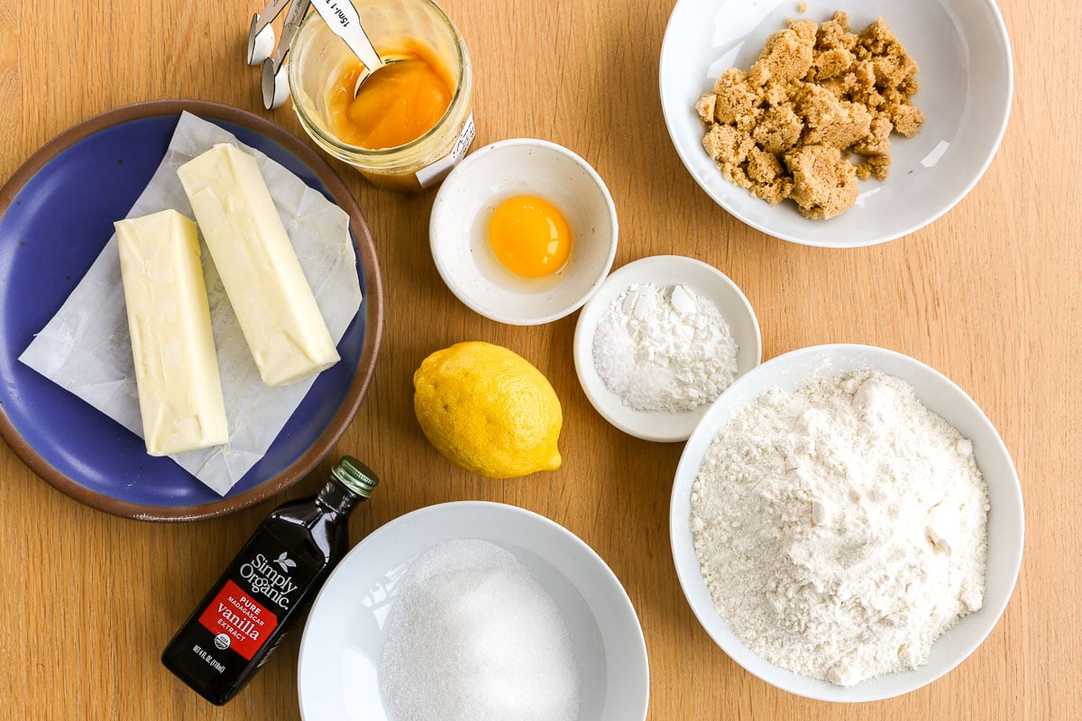 Baking ingredients on a table including butter, sugar, flour, brown sugar, egg, lemon, lemon curd, vanilla, and cornstarch.