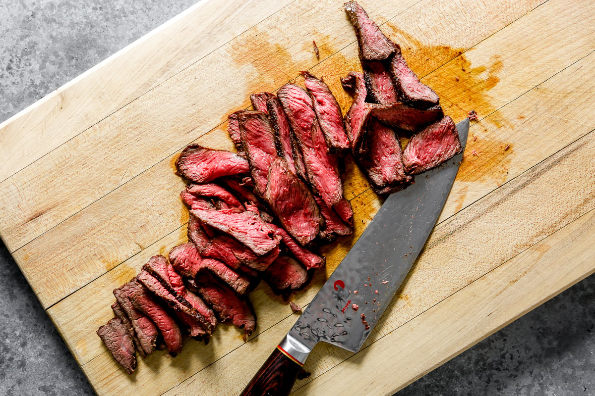 Medium-rare cooked steak thinly sliced on a wood cutting board.