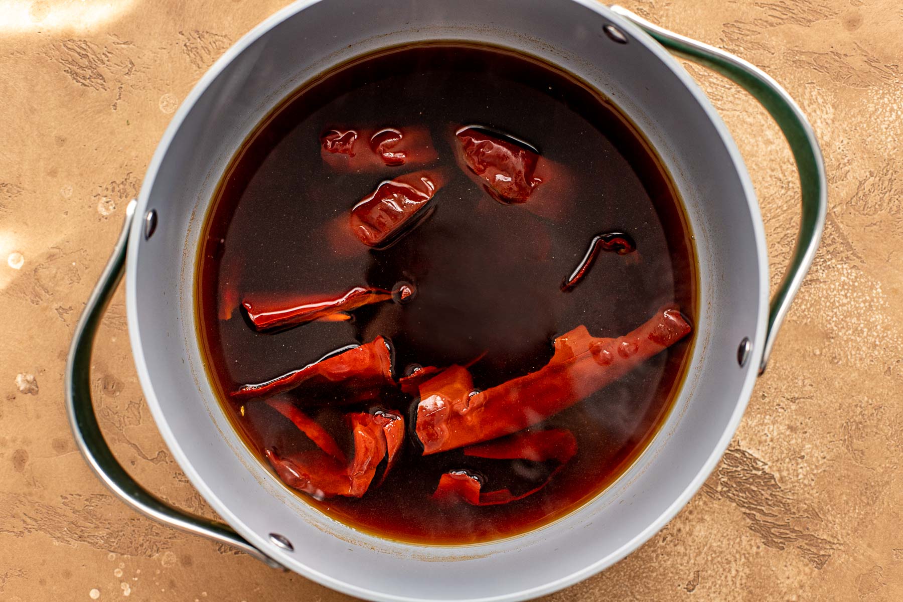 Dried chiles steeping in a pot of beef broth.