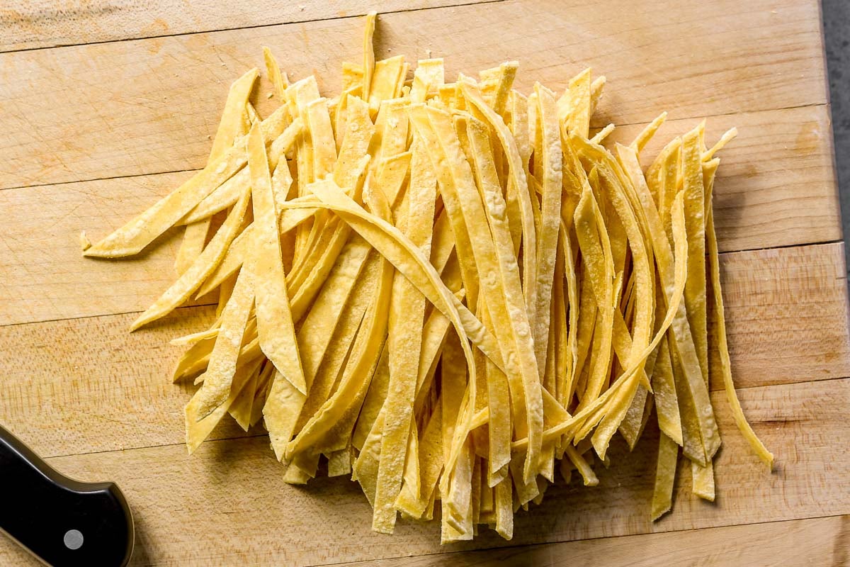 Thin strips of yellow corn tortillas on a wooden cutting board next to a black-handled knife.