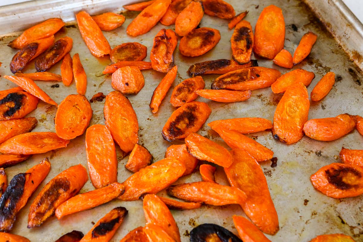 Sliced roasted carrots with browned edges on a metal baking sheet.