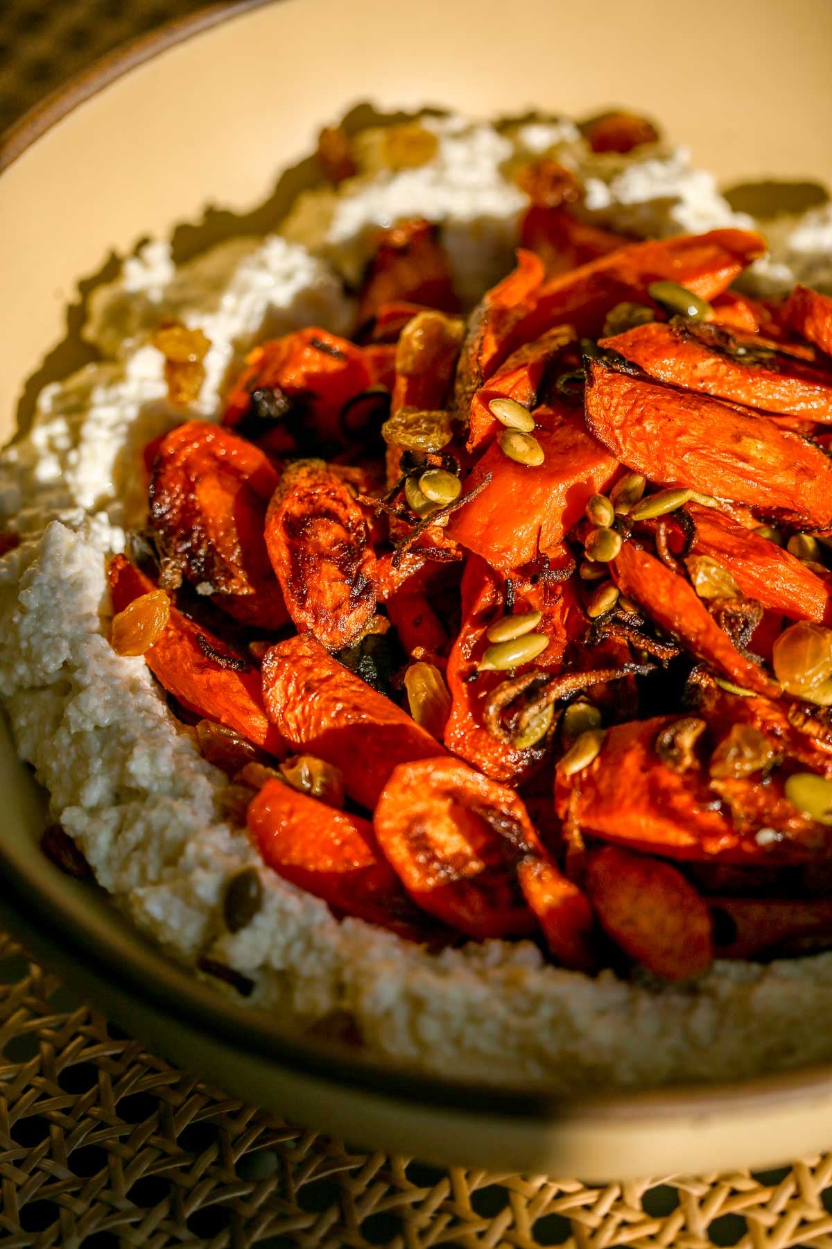 A bowl of whipped farmers cheese topped with roasted carrots, pepitas, and golden raisins, with a spoon on the side.
