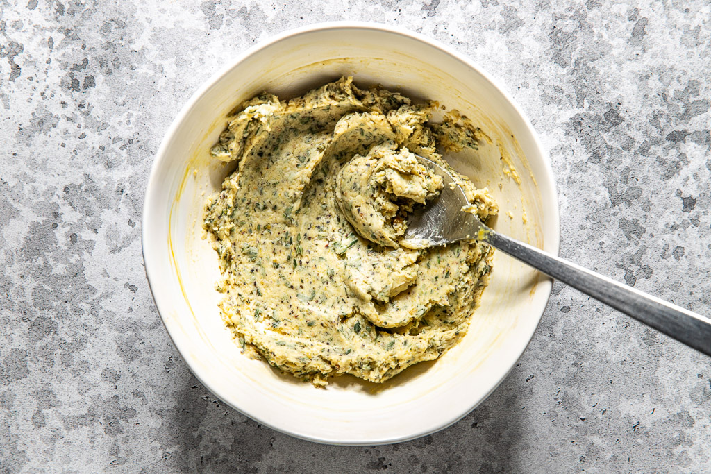 Herb butter in a small white mixing bowl with a silver spoon set in it.