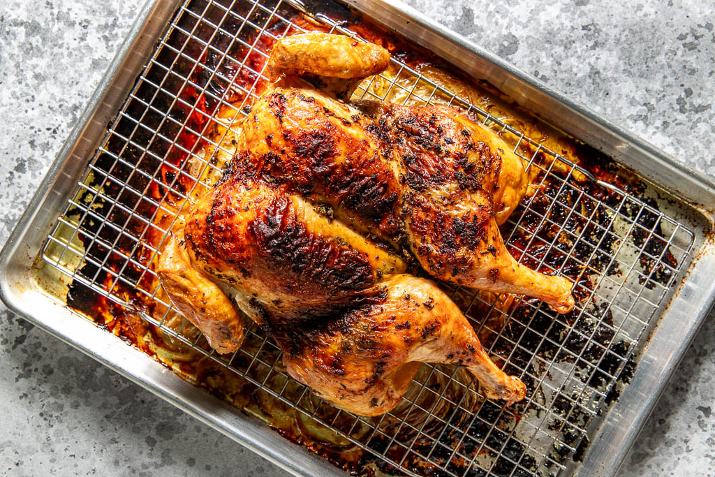 Roasted spatchcocked chicken with crispy skin on a wire rack over a baking sheet, sitting on a gray surface.