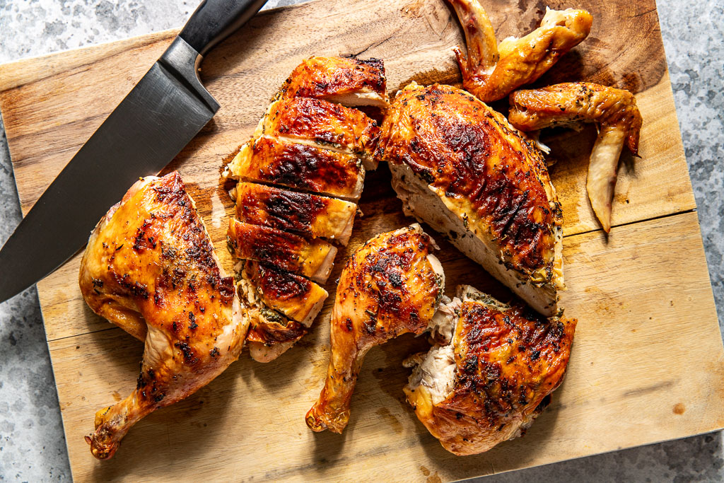Sliced roasted chicken on a wooden cutting board with a knife, showing crispy, golden-brown skin.