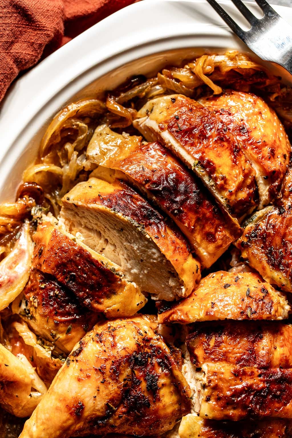 Close-up of roasted, sliced chicken breast with crispy, golden-brown skin on a white platter with caramelized onions.