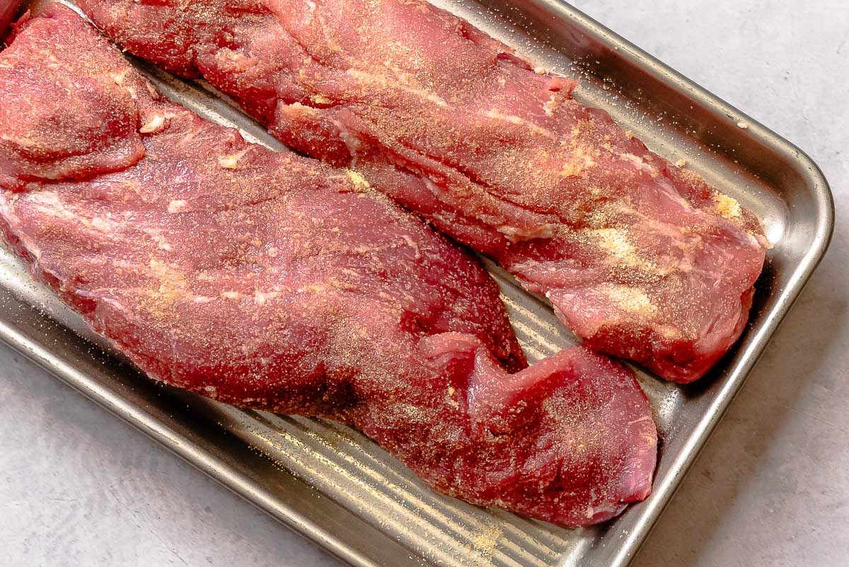 Trimmed pork tenderloin seasoned with salt and garlic powder on a sheet pan.