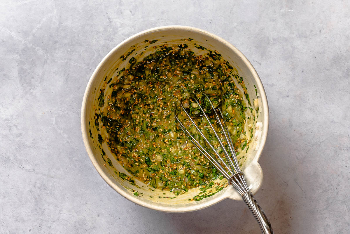 Green herb sauce in a white bowl with a small whisk.