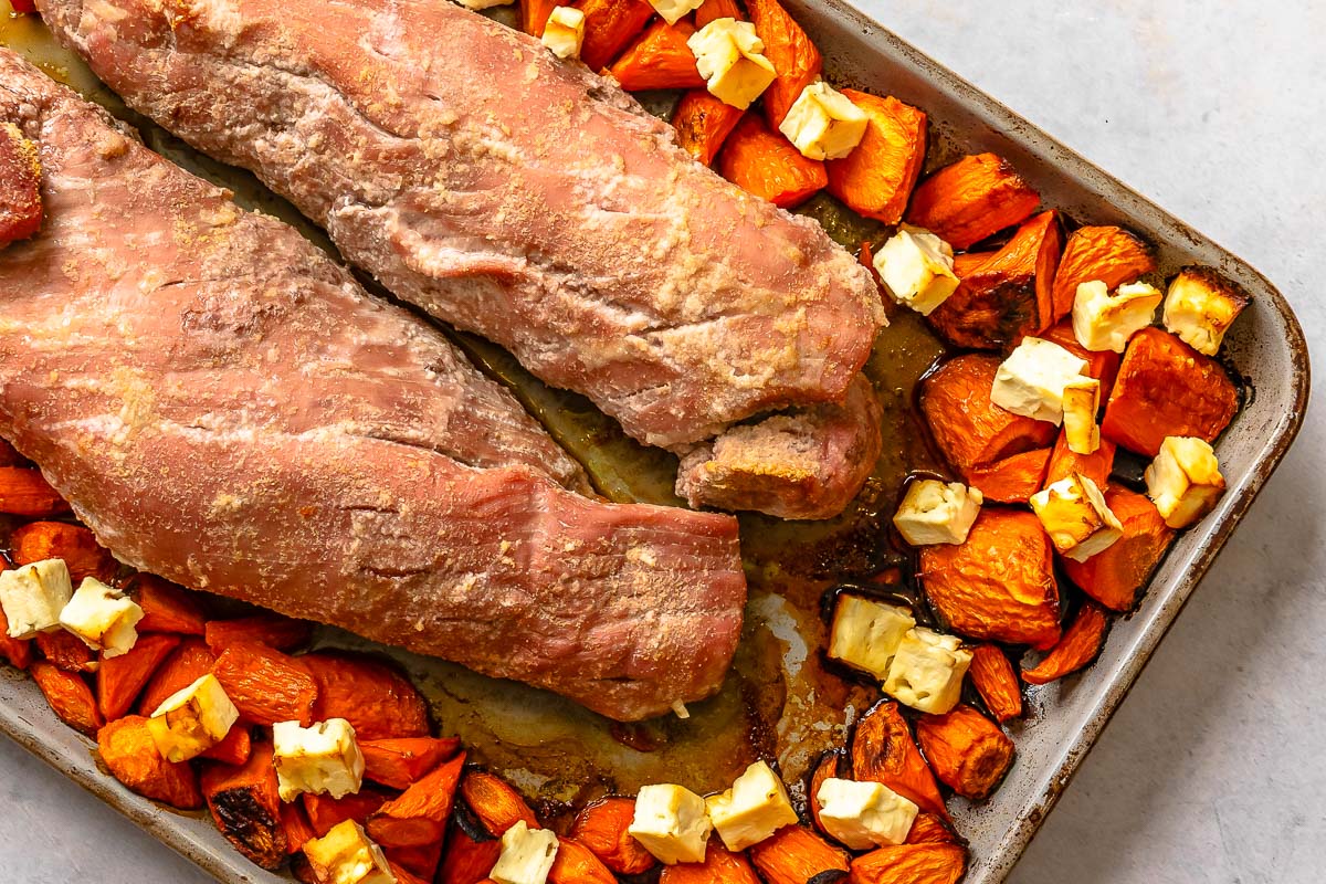 Two pork tenderloins on a baking sheet with cubed carrots and feta.