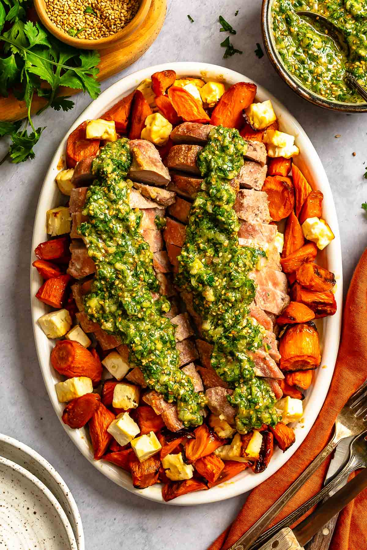 Sliced pork tenderloin with green sauce, roasted carrots, and cheese cubes on an oval platter.