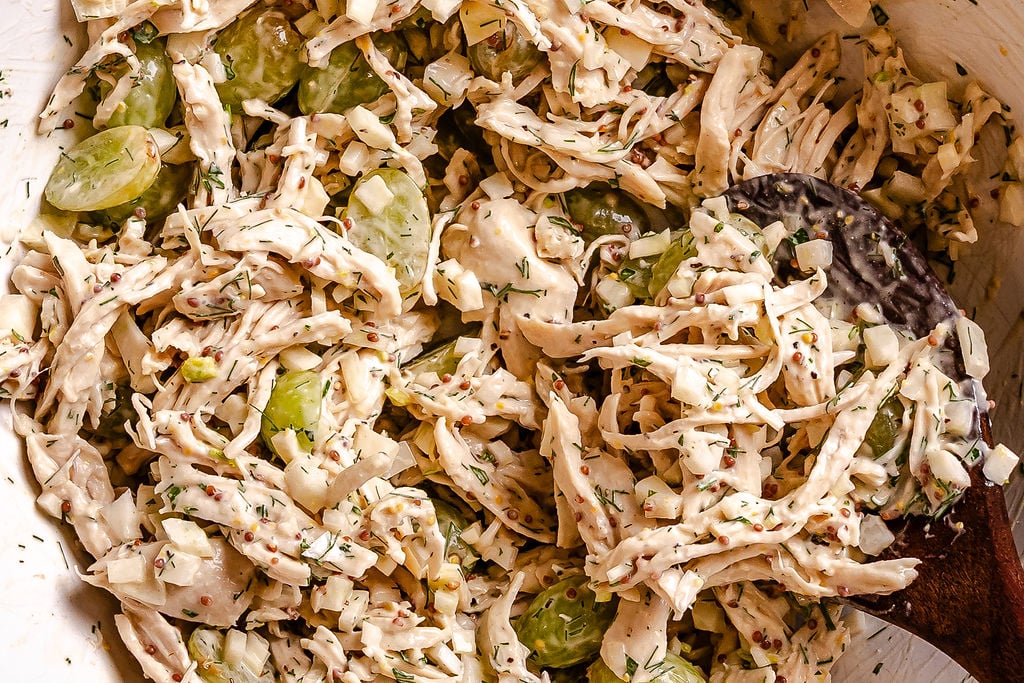 Chicken salad with green grapes, celery, herbs, and creamy dressing in a bowl with a spoon.