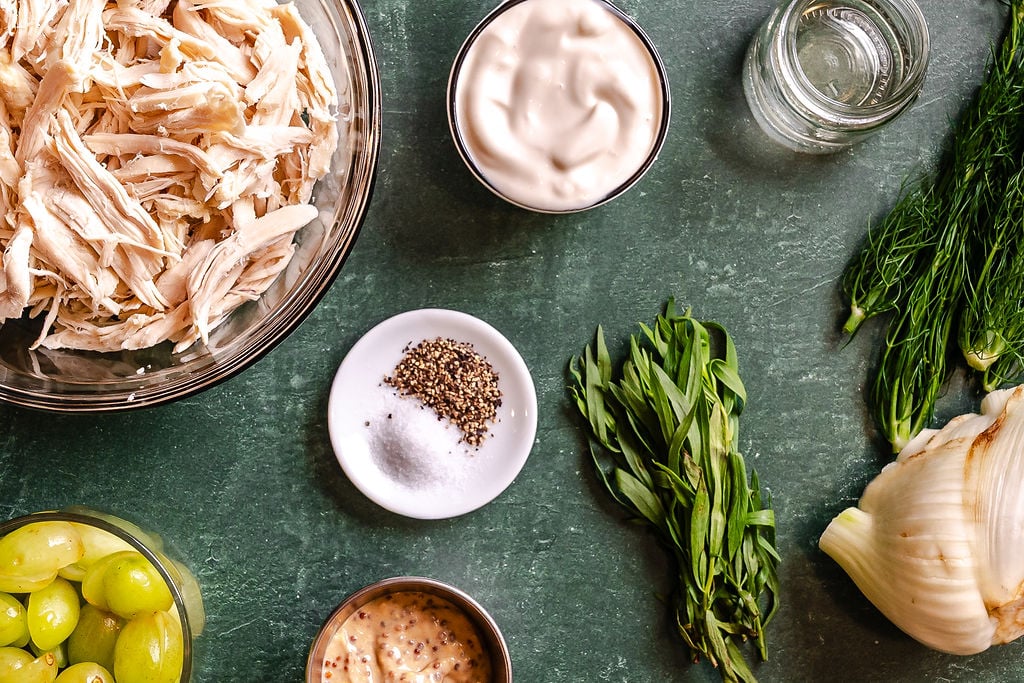 Shredded chicken, grapes, mayonnaise, salt, pepper, mustard, vinegar, fennel, dill, and tarragon on a green surface.