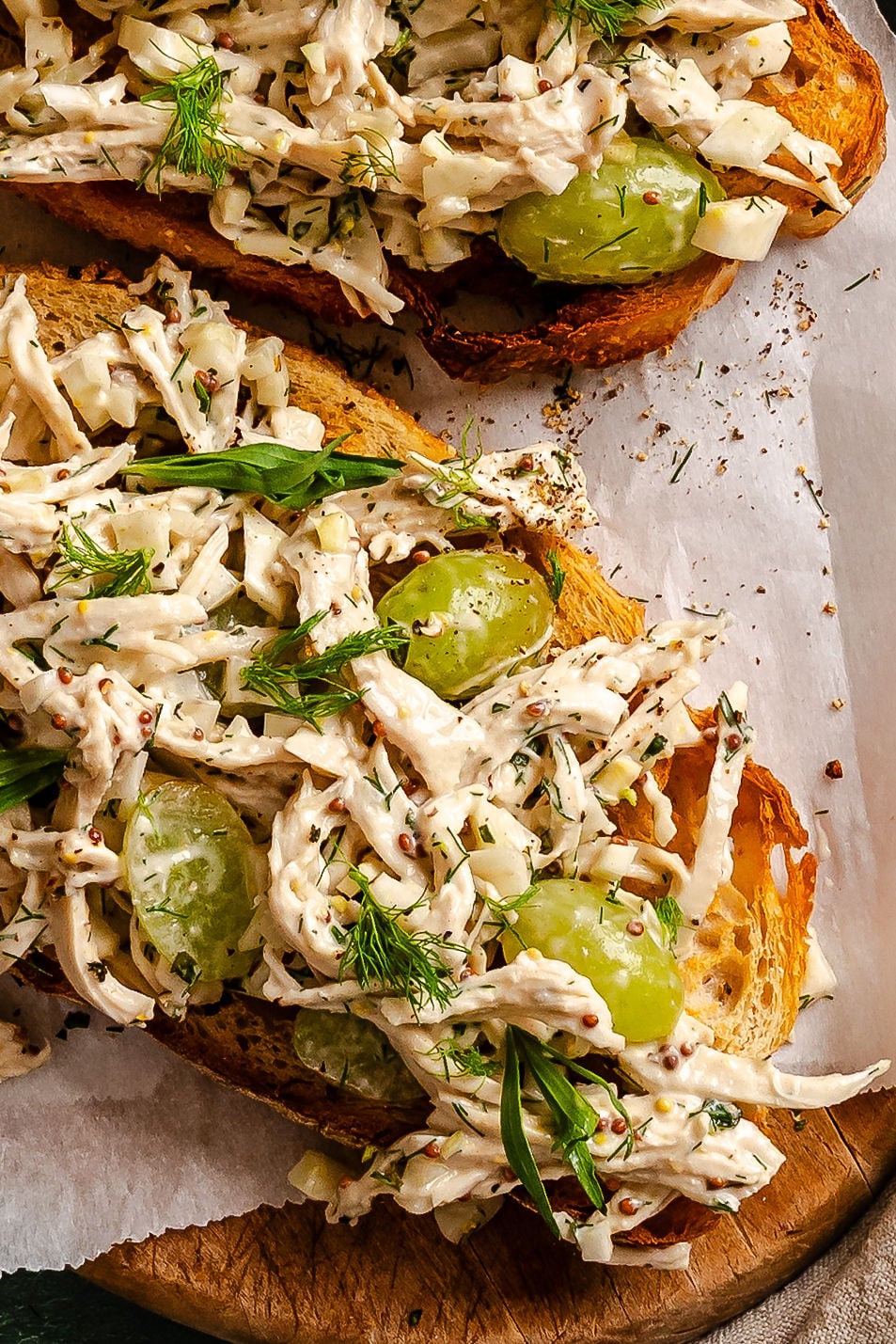 Open-faced sandwich with creamy chicken salad, green grapes, and herbs on toasted bread, served on parchment paper.