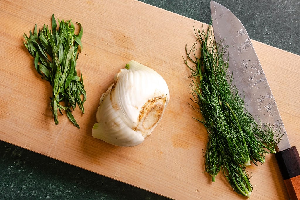 Fennel bulb., fennel fronds and fresh tarragon on a wood cutting board.