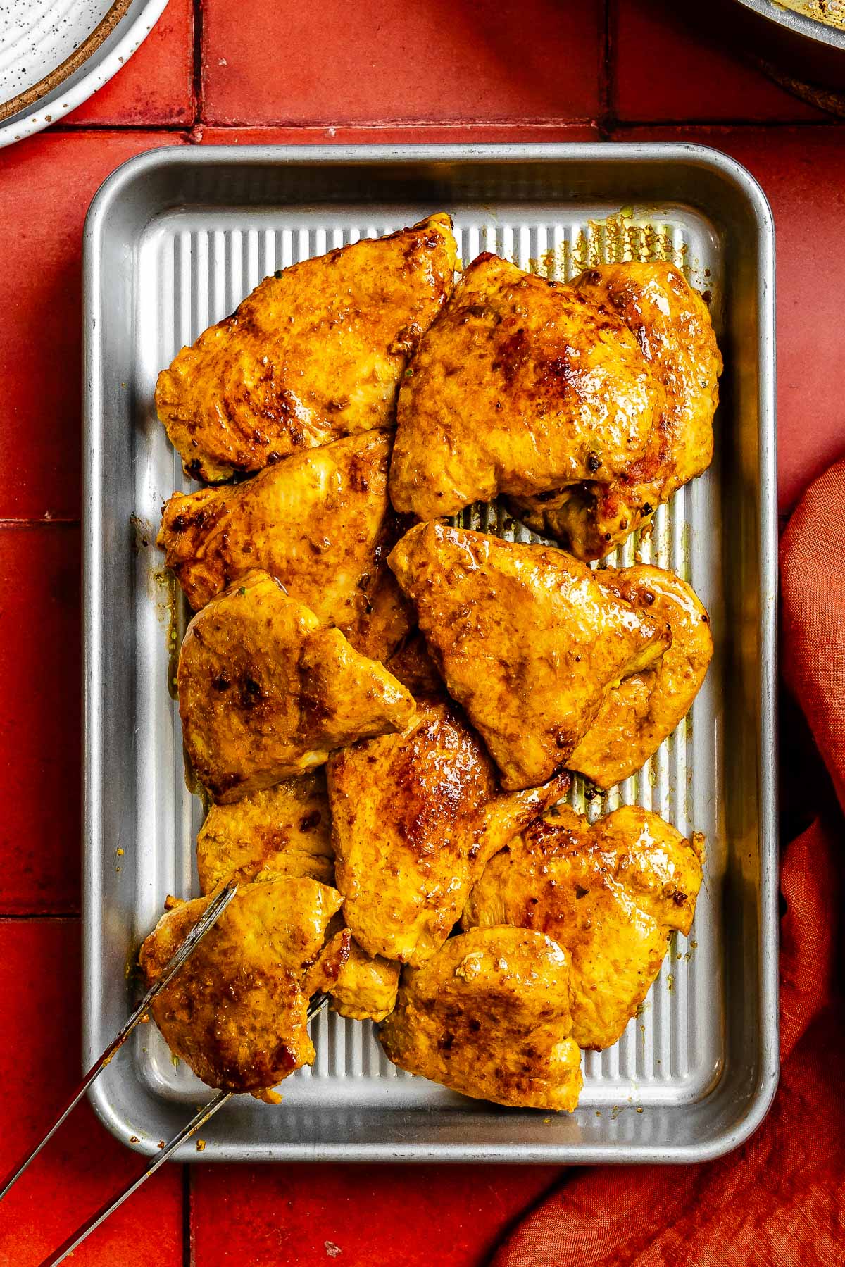 Curry marinated chicken breast, cooked and placed on a metal sheetpan.