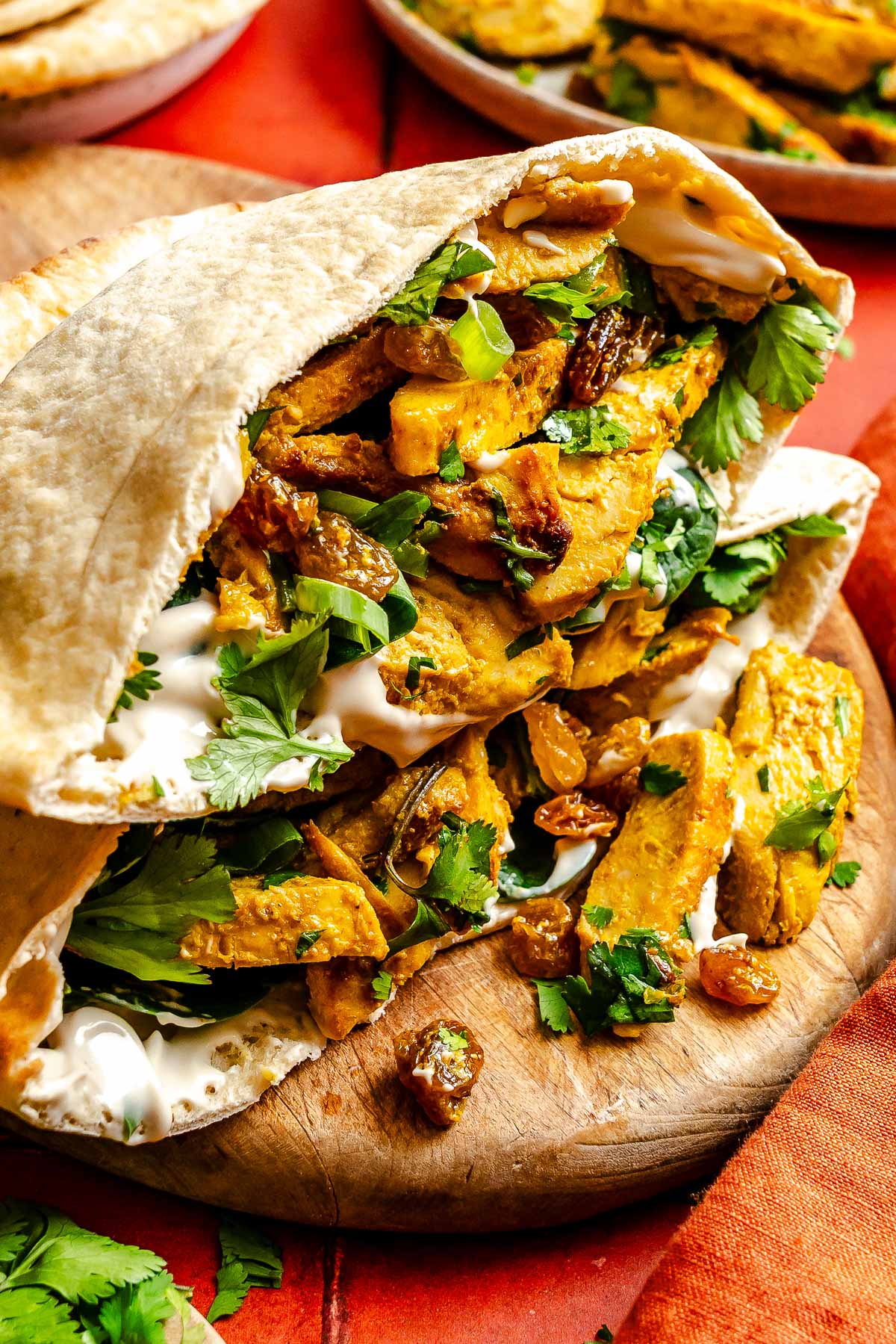 Pita stuffed with curried chicken, cilantro, and Greek yogurt on a wooden board with an orange napkin nearby.