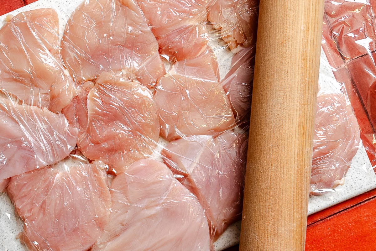 Chicken pieces pound out thin on a plastic cutting board.