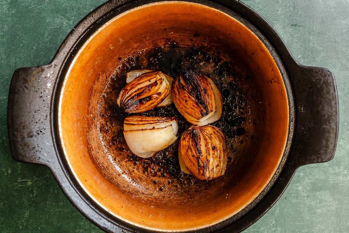 Four charred onion quarters in a brown pot resting on a dark green surface.
