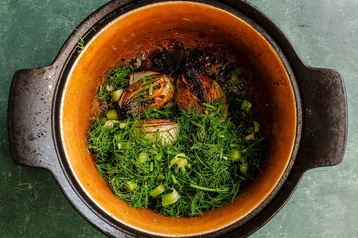 Onion wedges browning in a pot with sliced fennel stalks and chopped fronds scattered over top.