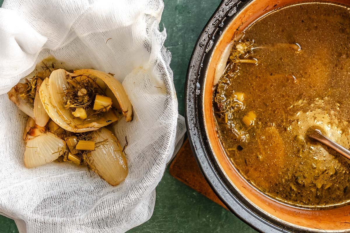Cooked onions, fennel and broth, ready to be strained through a cheesecloth set nearby.