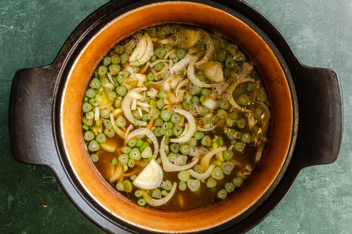 Sliced fennel bulb and fennel stalks cooking in a large brown pot of broth.