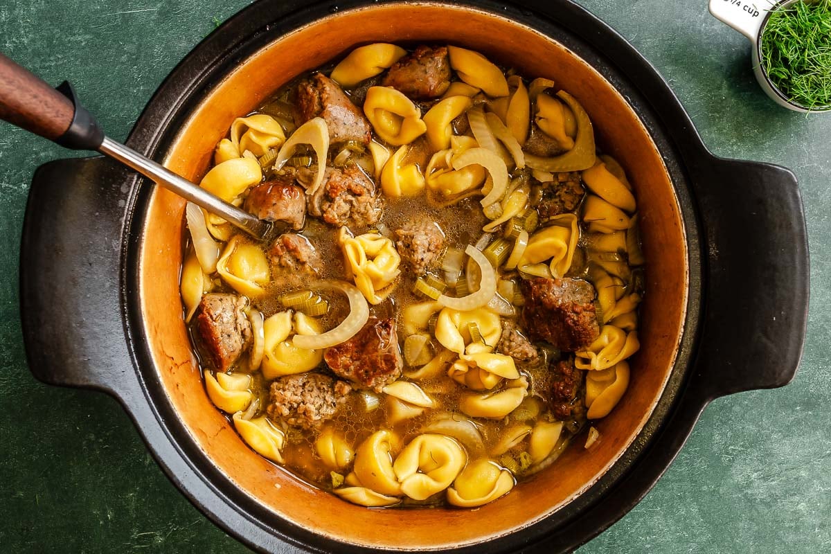A pot filled with tortellini, sausage, fennel and broth.