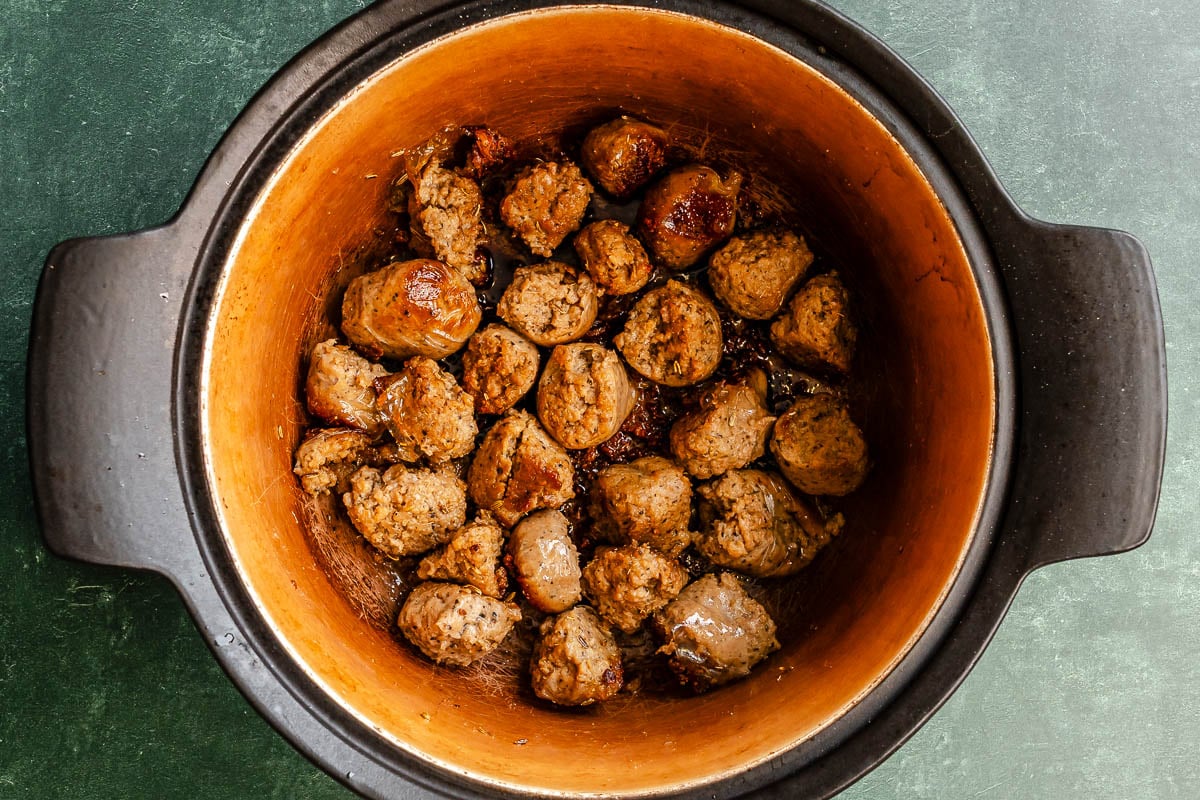 Chunks of browned sausage in a large brown pot.