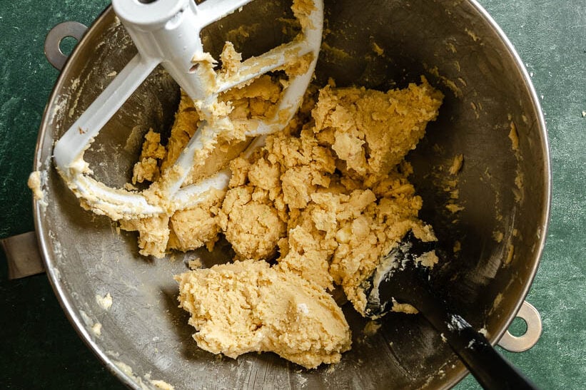 Cookie dough in a metal mixing bowl with a paddle attachment and spatula on a green countertop.