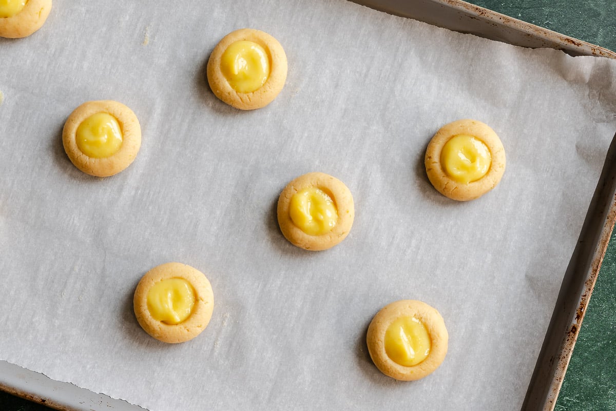Seven unbaked lime curd thumbprint cookies on a parchment-lined baking sheet.
