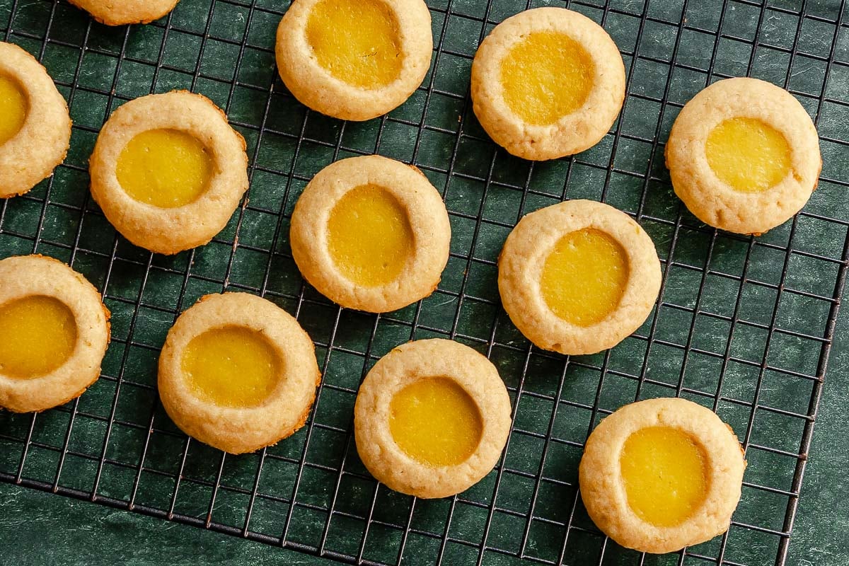 Lime thumbprint cookies cooling on a black wire rack over a green surface.