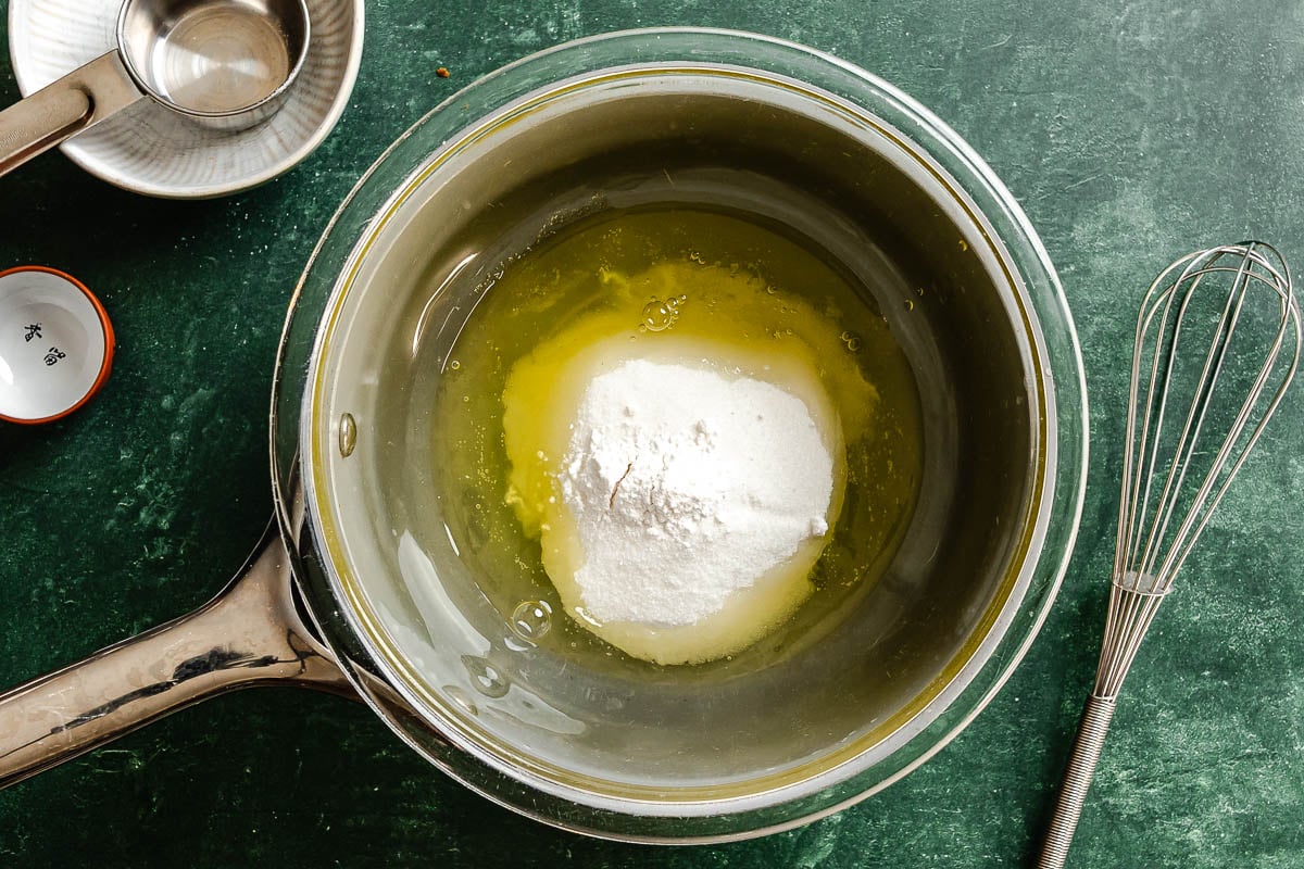 Egg white and sugar in a glass bowl set over a saucepan.