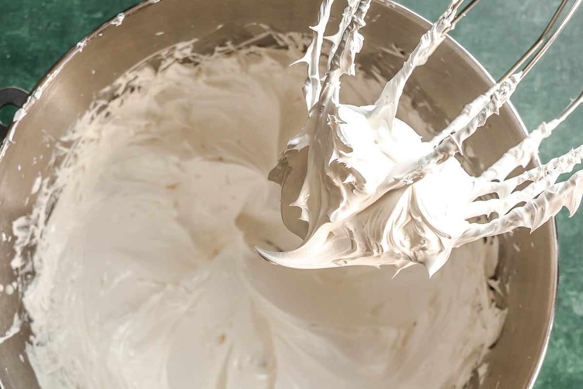 Whipped egg white meringue on a whisk set over a mixing bowl.