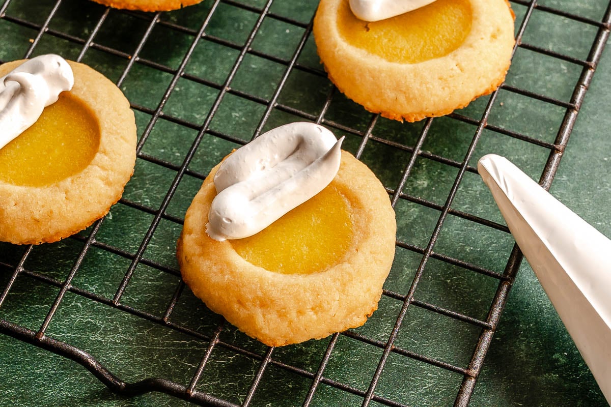 Round cookies with yellow centers and toasted meringue on top, cooling on a wire rack over a green surface.