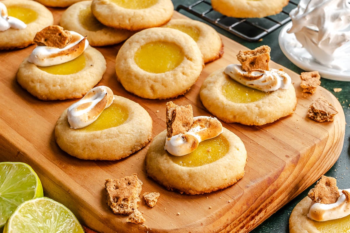 Lime thumbprint cookies topped with toasted meringue and graham cracker pieces on a wooden board.