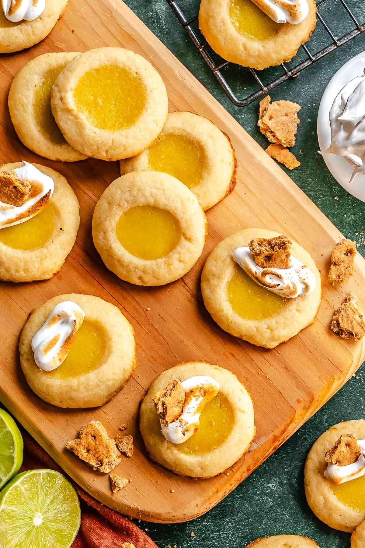 Lime thumbprint cookies topped with toasted meringue and graham cracker pieces on a wooden board.
