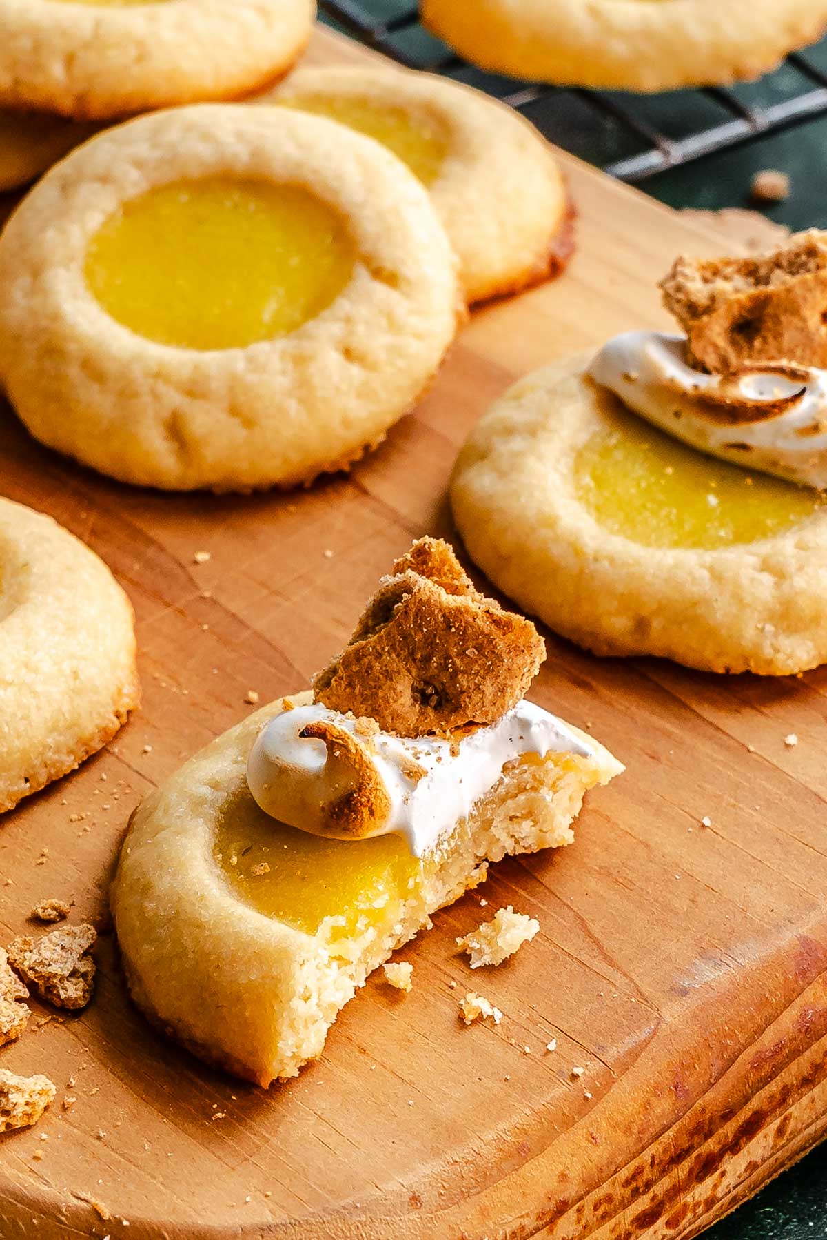 Lime thumbprint cookies topped with toasted marshmallow and graham cracker pieces on a wooden board.