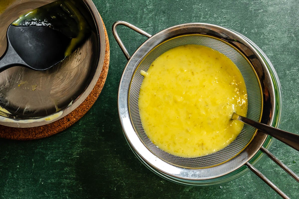 Lime curd straining through a fine mesh sieve with an empty saucepan set nearby.