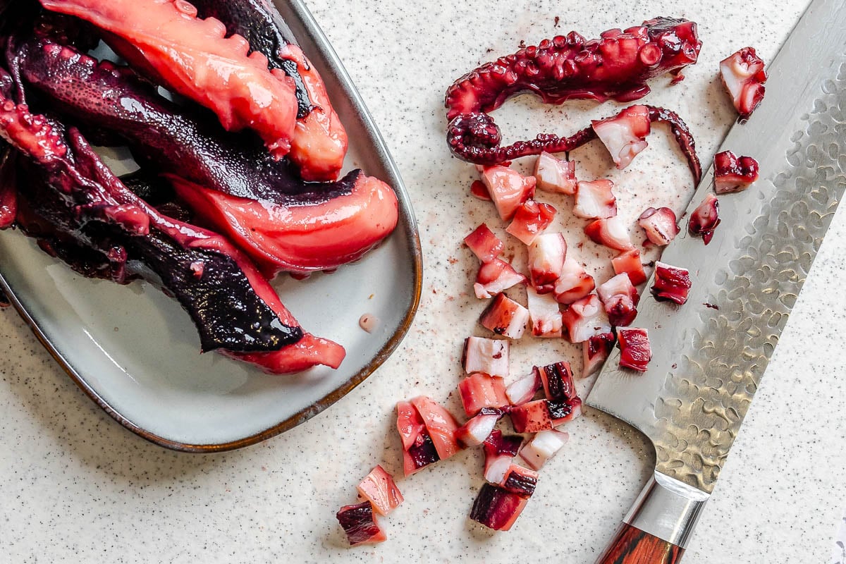 Chopped octopus tentacles on a cutting board with a knife and a plate of whole tentacles nearby.