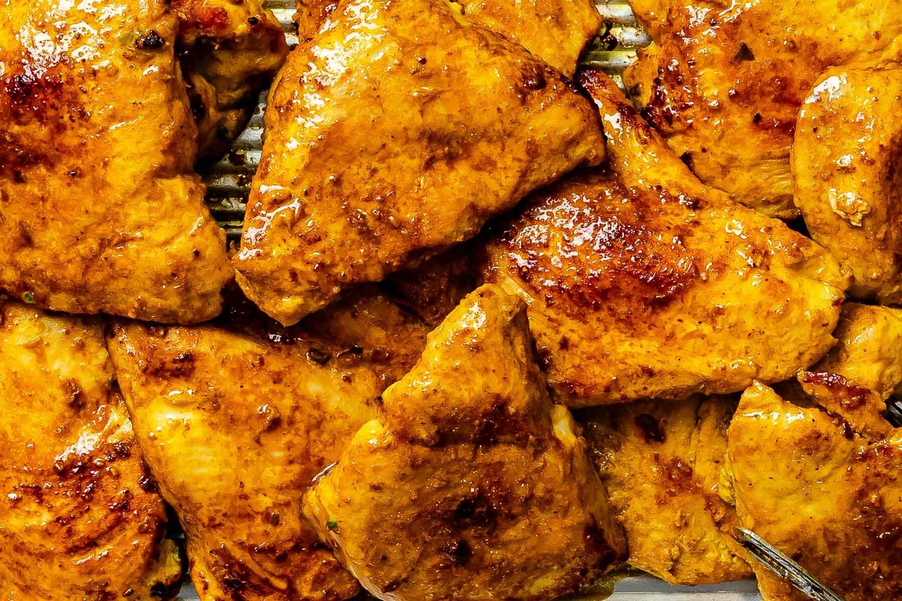 Curry marinated chicken breast, cooked and placed on a metal sheetpan.