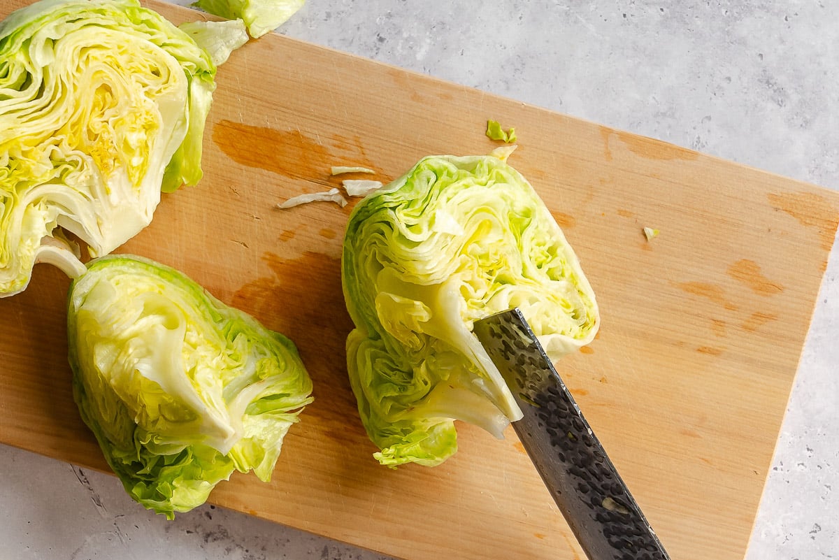 A knife cutting a head of lettuce into wedges on a wooden cutting board.