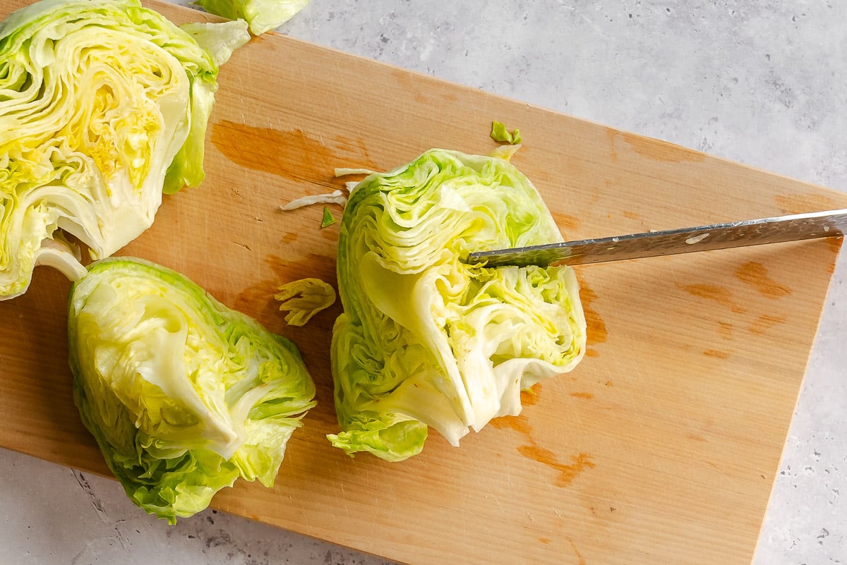 A knife cutting a head of lettuce into wedges on a wooden cutting board.