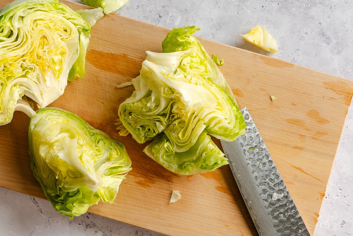A knife cutting a head of lettuce into wedges on a wooden cutting board.