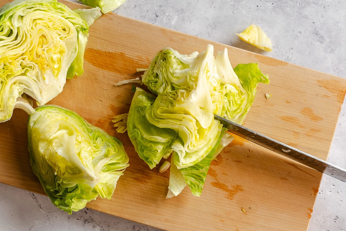 A knife cutting a head of lettuce into wedges on a wooden cutting board.