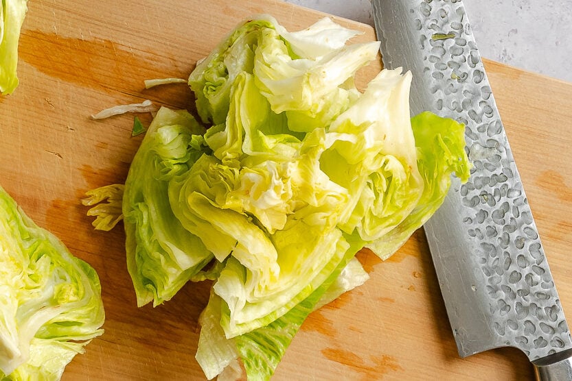 A knife cutting a head of lettuce into wedges on a wooden cutting board.