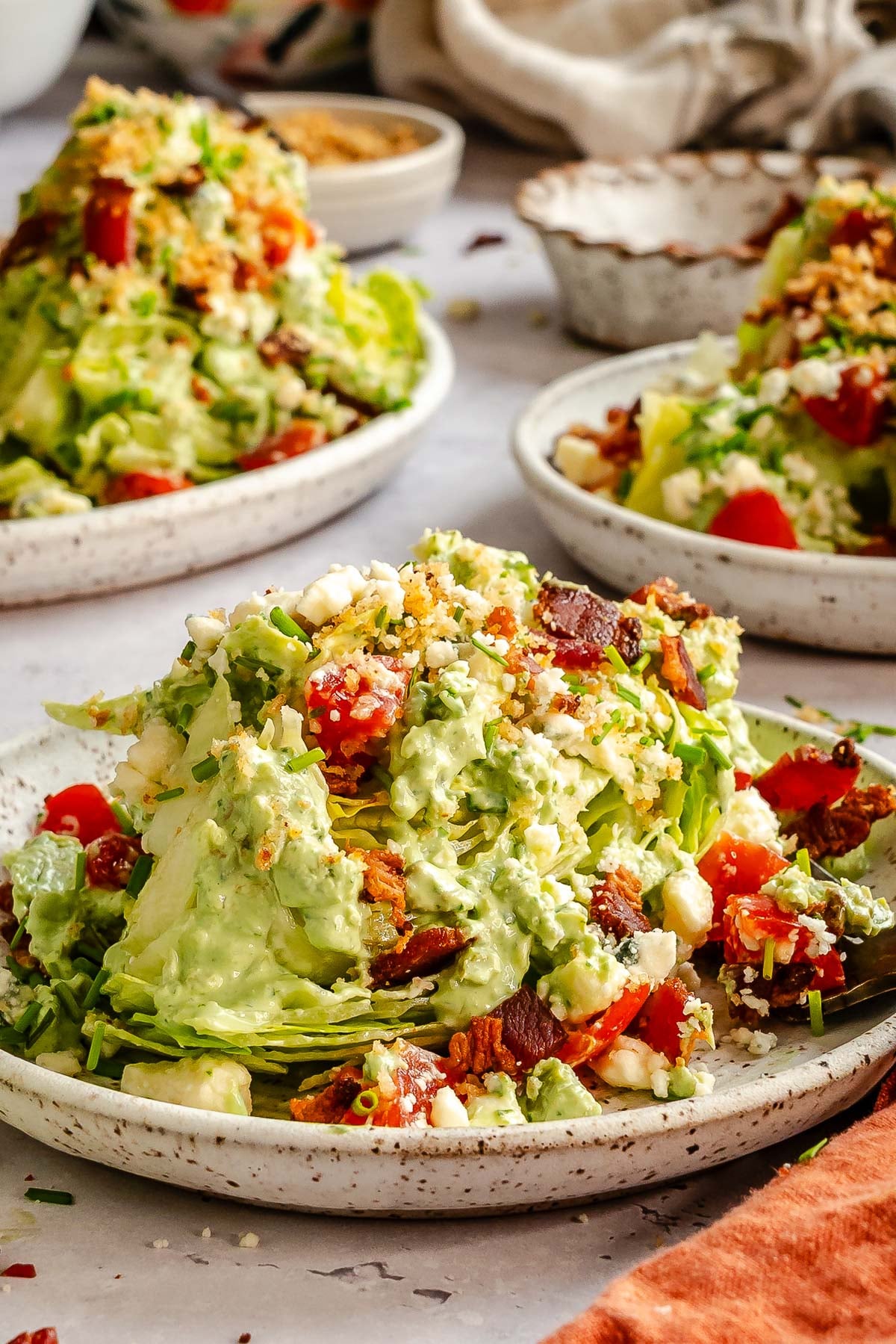 Wedge salad topped with creamy dressing, bacon, tomatoes, and crumbled cheese on a speckled plate.